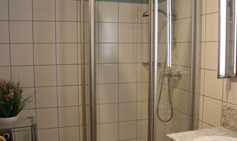 A modern bathroom with a glass shower cabin. The walls are tiled, and there is a sink with a mirror.
