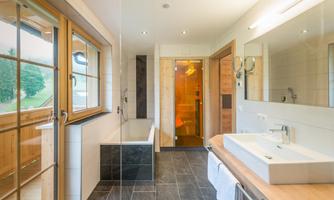 A modern bathroom with a bathtub, shower, and a large window. The decor is bright and inviting, featuring stylish tiles and wooden details.