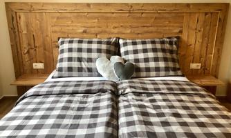 A cozy bedroom with a wooden headboard and checked bedding. Two heart-shaped pillows are lying on the bed.