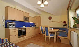 A modern kitchen with wooden cabinets and a blue wall. There is a dining area with a table and benches.