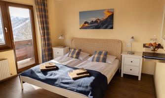 A cozy bedroom with a double bed and modern furniture. Large windows offer a view of nature and let in plenty of light.