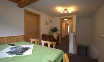 A cozy room with a table and chairs, showing a staircase and additional doors. The walls are light, and there are plants on the table.