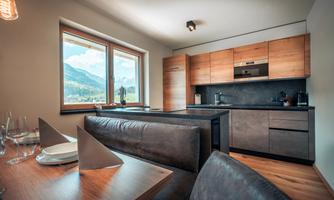 Modern kitchen with wooden details and large windows. Mountains can be seen in the background.