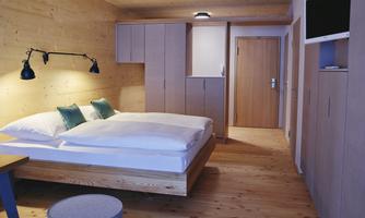 A modern bedroom with wood paneling and a comfortable bed. The room features simple furniture and a calm atmosphere.