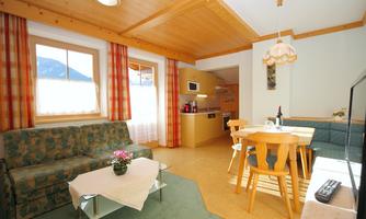 A cozy living space with a green couch and dining area. The room has large windows with a view of the mountains and a bright, welcoming atmosphere.