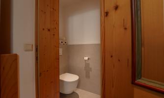 A small toilet with a modern ceramic toilet and gray walls. The room is bright and has a wooden frame on the door.