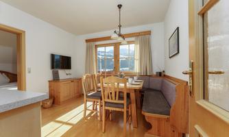 A cozy dining area with a wooden table and chairs. Large windows offer a view of the mountains and natural light.