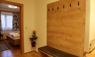A cozy hallway with a wood panel and coat hooks. In the background, a bedroom with a double bed is visible.