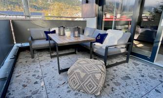 A cozy terrace with modern furniture and a view of the mountains. The table is surrounded by two comfortable armchairs and a pouf.