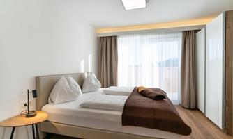 A modern bedroom with a double bed and two pillows. The large windows provide plenty of daylight and a view outside.