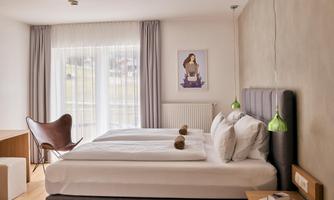 A modern bedroom with two beds and a desk. Large windows provide plenty of daylight and a pleasant atmosphere.