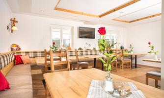 A cozy restaurant with wooden chairs and tables. Fresh flowers are on the tables, and a TV hangs on the wall.