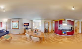 A modern living and dining room with an open kitchen. The furniture is bright and friendly, with wooden flooring and large windows.