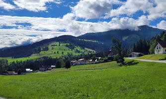 A picturesque landscape with green hills and dense forests. In the background, the mountains and a blue sky with clouds can be seen.
