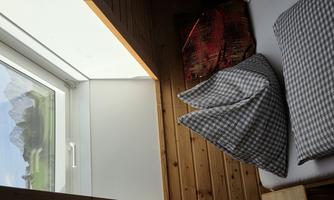 A cozy room with a skylight through which the mountains are visible. There are large pillows on the bed and warm wooden paneling.