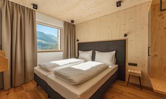 A modern bedroom with a double bed and large windows. The walls are made of wood and the decor is minimalist and cozy.