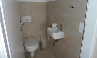 A small bathroom with modern tiles. There is a toilet, a small sink, and a minimalist decor.