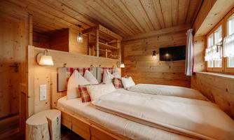 A cozy bedroom with wooden paneling and two single beds. Large windows let in plenty of daylight and provide a warm atmosphere.