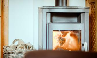 A modern fireplace stove with a blazing fire. Next to it is a basket with wood.