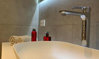 A modern bathroom with an elegant, white sink and a contemporary faucet. In the background, towels and personal care products in shades of red are visible.
