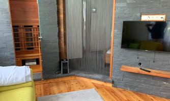 A modern living space with a comfortable sofa and a TV on the wall. In the background, there is a transparent partition and access to another room.