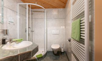 A modern bathroom with a glass shower and sink. The walls are tiled in a light color, and green towels provide a splash of color.