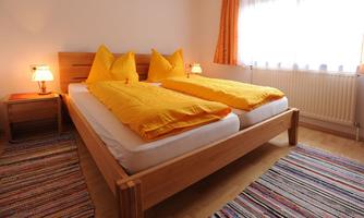 A cozy bedroom with a double bed and bright yellow bedspreads. The room is bright and friendly with a colorful carpet and warm light.
