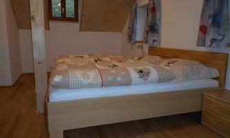A cozy bedroom with a wooden bed and a large comforter. The walls are light, and there are windows with curtains.