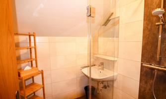 A modern bathroom with a shower cabin and a small sink. Next to the shower, there is a wooden shelf.