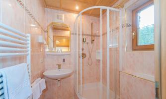 A modern bathroom with a shower cubicle and bright pink tiles. The space is well-lit and features a round mirror and towels.