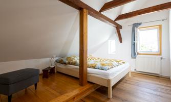 A cozy bedroom with a double bed and wooden floor. Large windows let in plenty of daylight.
