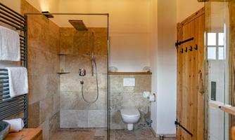 A modern bathroom with a glass shower and a white toilet. The walls are clad with stone slabs, and there are wooden details.