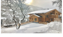 A charming wooden house in the snow with a sunny sky in the background. Surrounded by snow-covered trees and a picturesque winter landscape.