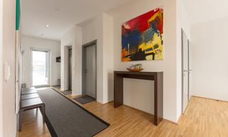 A bright hallway with wooden flooring and modern gray doors. A colorful painting hangs on the wall, and an elegantly designed table is in the room.