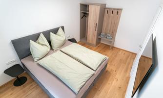 A cozy bedroom with a large bed. Next to the bed is a wardrobe and a coat rack.