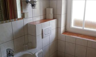 A small bathroom with a sink and a toilet. The room has bright tiles and a window that lets in daylight.