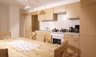 A cozy kitchen with wooden cabinets and a large dining table. The countertop is tidy and equipped with kitchen appliances.