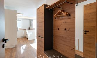 A modern entrance area with a wooden cupboard and a large window for plenty of daylight. The floors are made of light wood, which creates a friendly atmosphere.