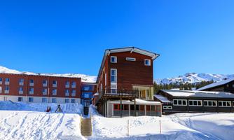 A hotel building in a snow-covered landscape with a blue sky in the background. The surroundings show mountains and a calm winter atmosphere.