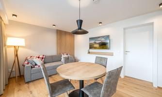 A modern living room with a round wooden table and elegant chairs. A cozy sofa and a floor lamp create an inviting atmosphere in the space.