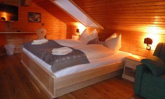 A cozy bedroom with wooden paneling and a double bed. There is soft lighting and a television on the wall.