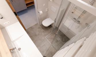 A modern bathroom with a shower and a toilet. The walls are light and the floor is tiled in gray.