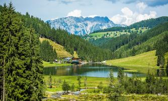 A picturesque landscape with a calm lake and green meadows. In the background, mountains and forests can be seen.