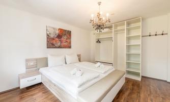 A modern bedroom with a large bed and bright wooden floor. There is a wardrobe and an appealing ceiling light.