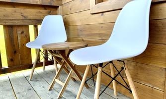 Two white chairs sit next to a small table on a wooden porch. The walls are made of wood and create a cozy atmosphere.