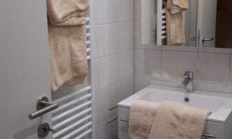 A modern bathroom with a towel warmer and a sink. The walls are tiled and a mirror hangs above the sink.