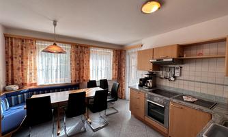 A modern kitchen with a dining table and black chairs. Large windows provide plenty of daylight and an inviting atmosphere.