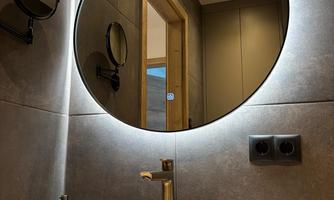A modern bathroom with a round mirror and a stylish washbasin. Towels are neatly arranged on a wooden board.