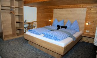 A cozy room with a large bed and blue pillows. There is a wooden wardrobe and a table with chairs.