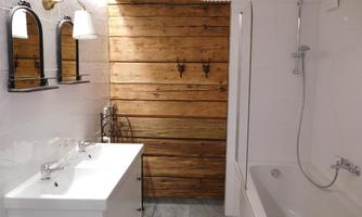 A modern bathroom with two sinks and a bathtub. The walls are partially covered with wood, which adds a warm touch.